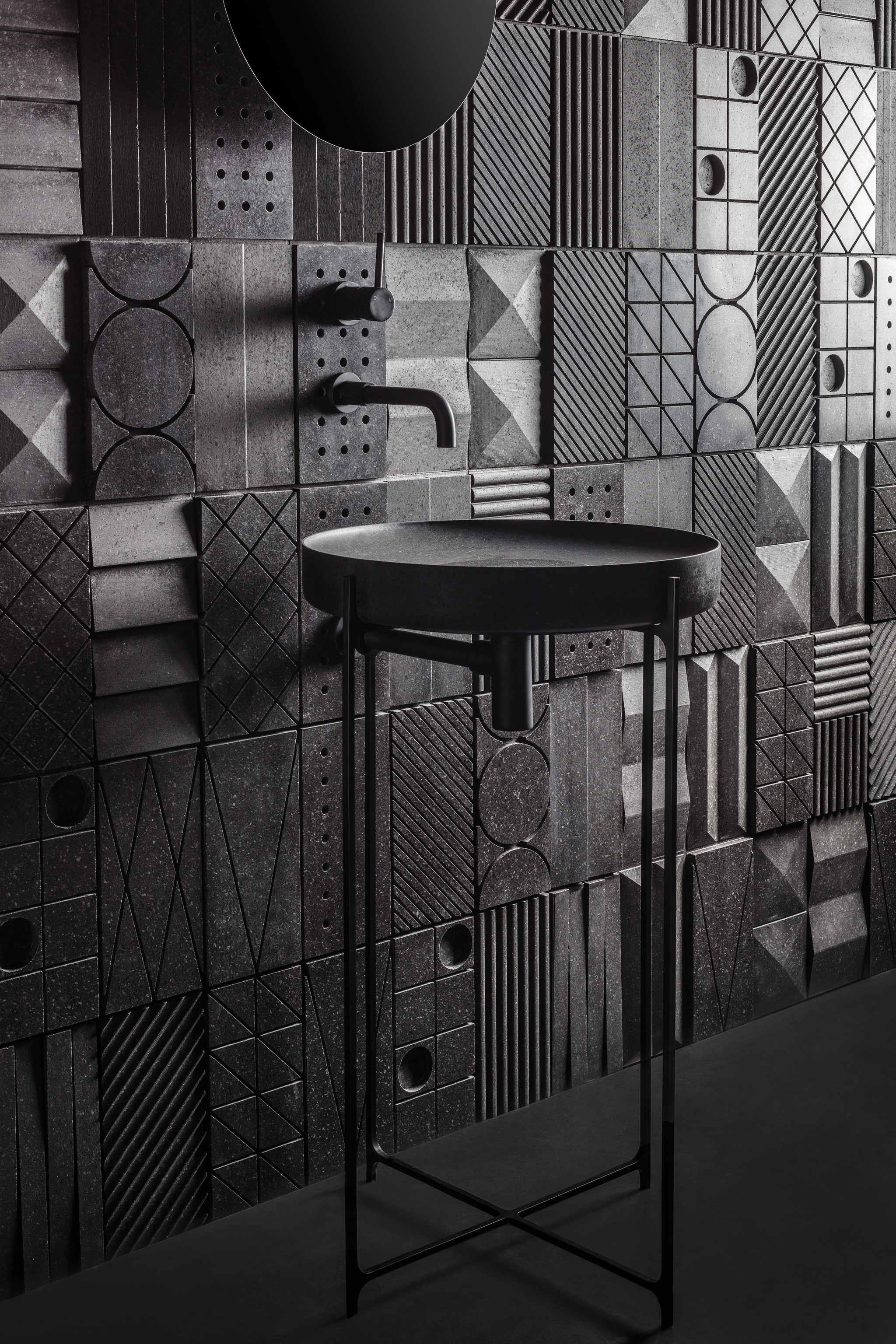 Modern bathroom featuring black geometric 3D wall panels with a structured, textured surface. These gypsum 3D panels by Kandes create a striking visual effect, enhancing the depth and contrast of the monochrome interior. The non-combustible, eco-conscious wall cladding pairs seamlessly with the minimalist black sink and matte fixtures